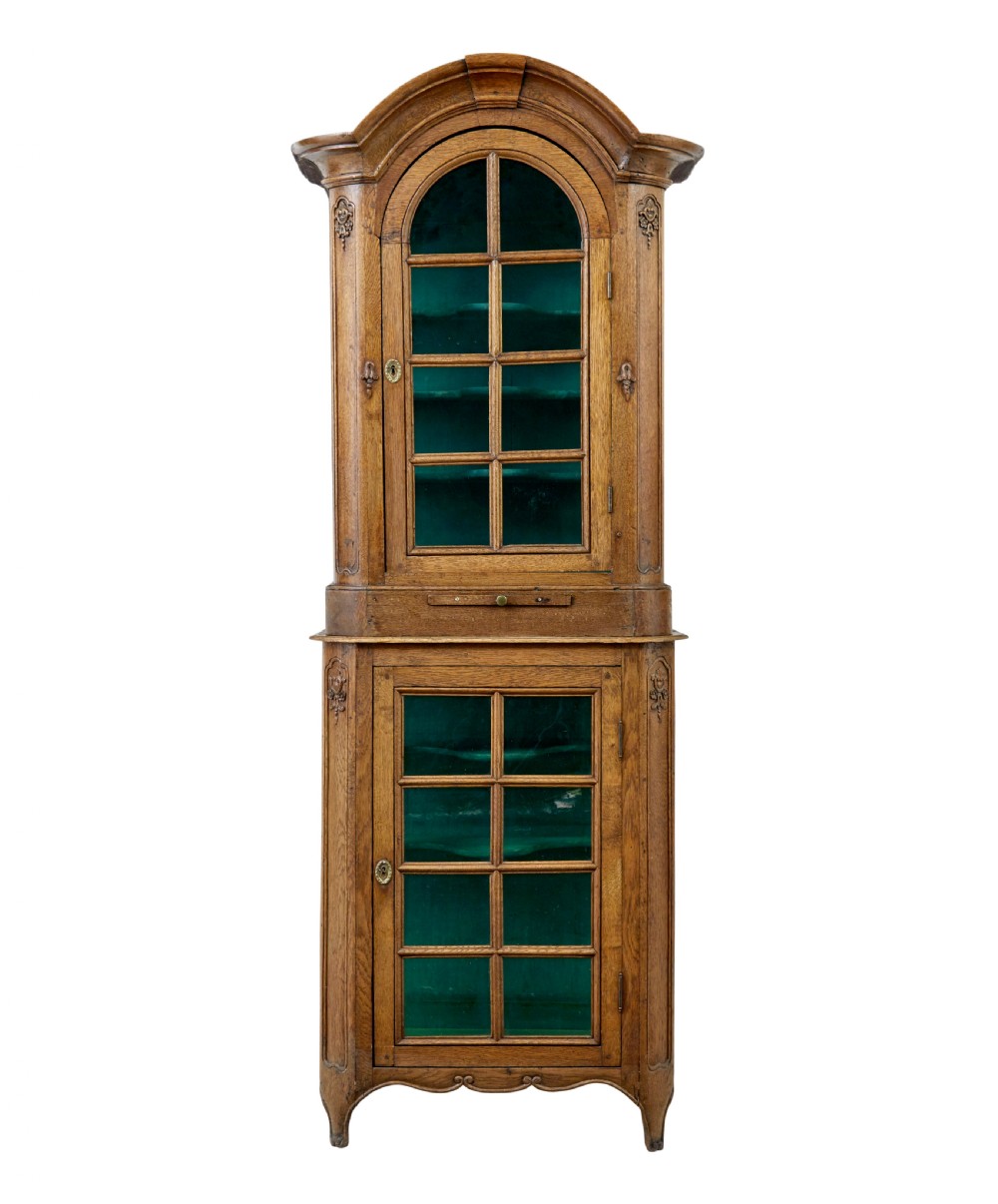 A mid-19th-century carved oak display cabinet featuring glazed doors, arched pediment, and green fabric interior lining. View II