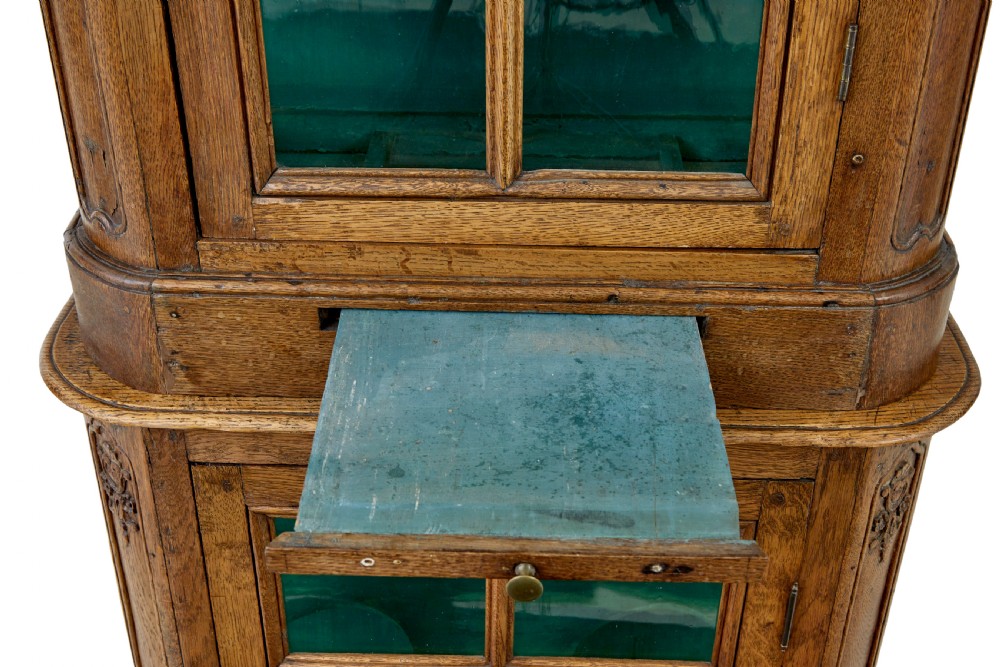 A mid-19th-century carved oak display cabinet featuring glazed doors, arched pediment, and green fabric interior lining. View VII