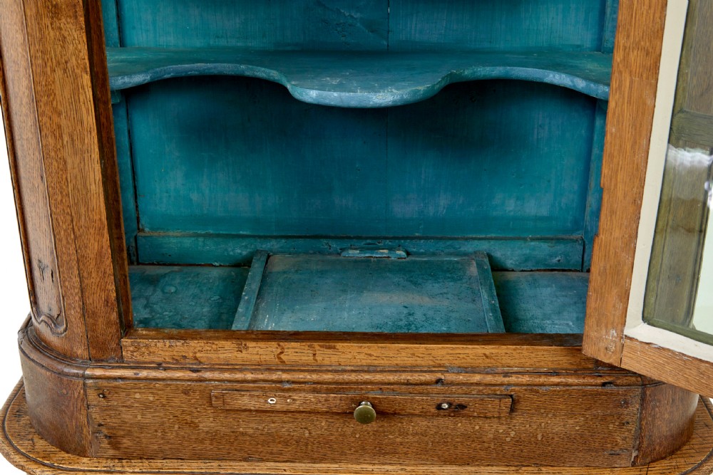A mid-19th-century carved oak display cabinet featuring glazed doors, arched pediment, and green fabric interior lining. View VIII