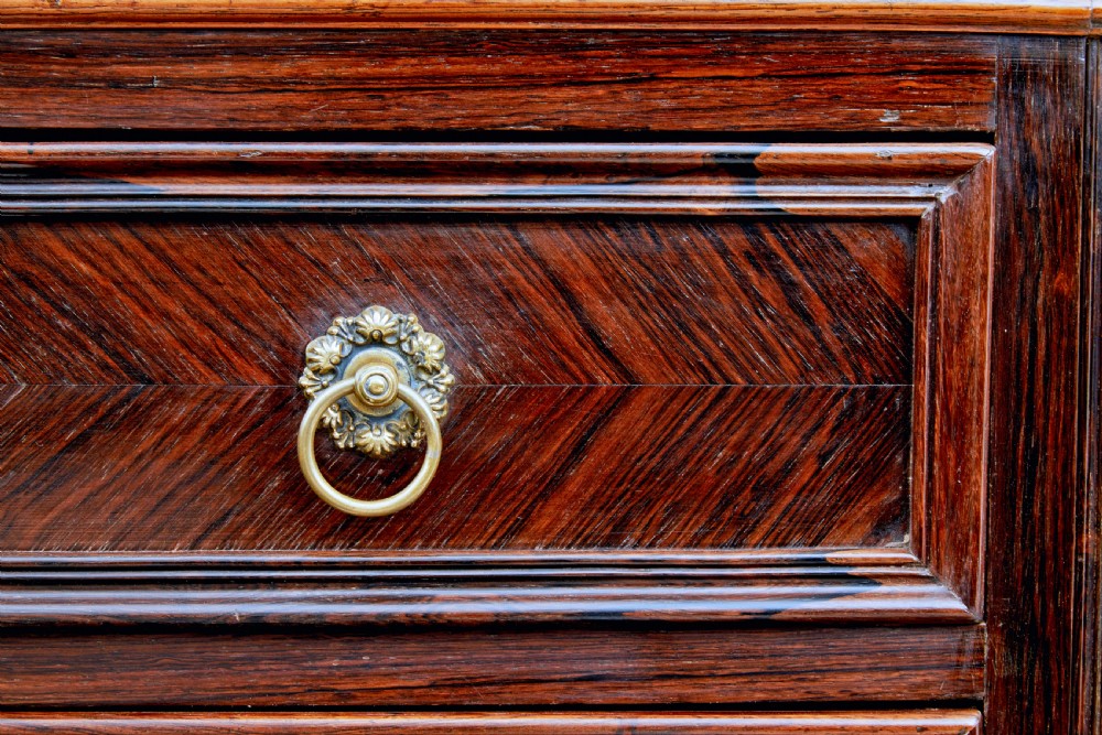 A nineteenth-century French palisander chest of drawers featuring chevron grain veneering, decorative brass drop handles, and a faux marble top. View X
