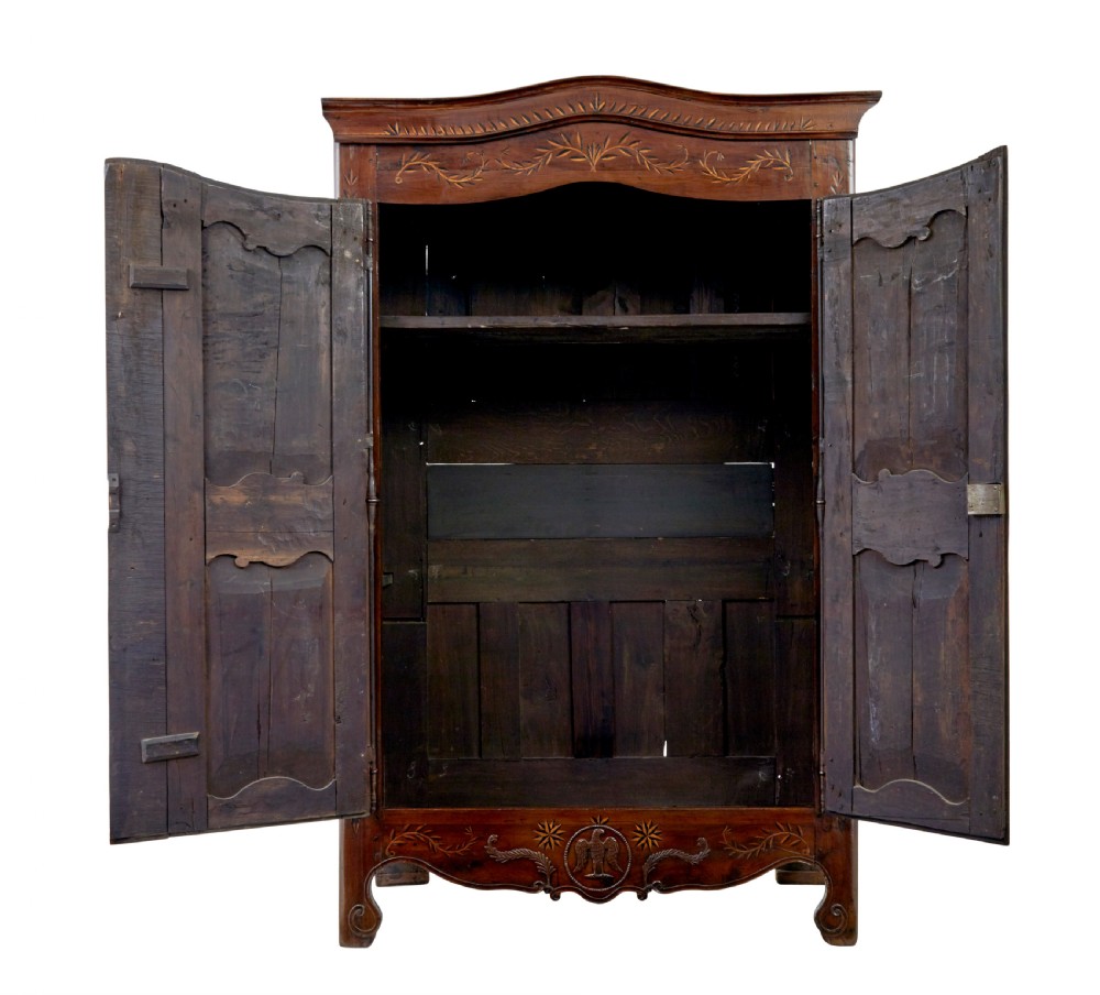 An 18th-century French armoire in warm brown yew and chestnut wood featuring carved foliate inlay, arched panel doors, and long iron escutcheons. View II