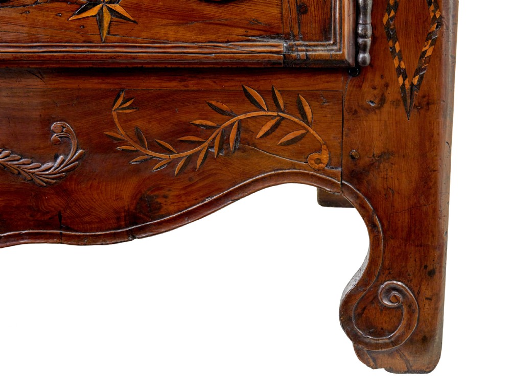 An 18th-century French armoire in warm brown yew and chestnut wood featuring carved foliate inlay, arched panel doors, and long iron escutcheons. View VII