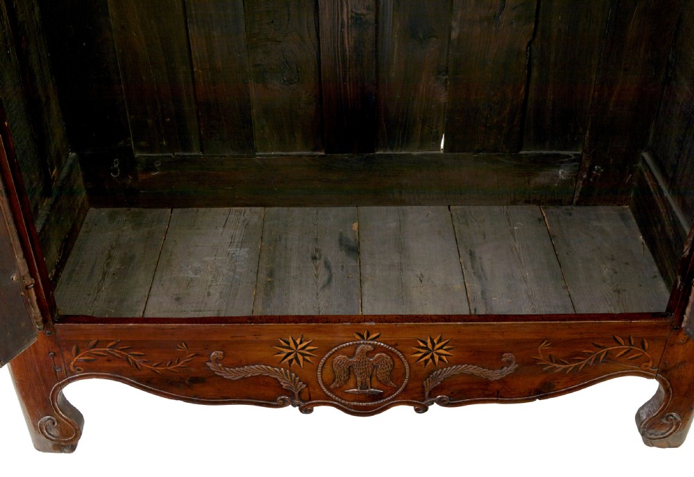 An 18th-century French armoire in warm brown yew and chestnut wood featuring carved foliate inlay, arched panel doors, and long iron escutcheons. View VIII