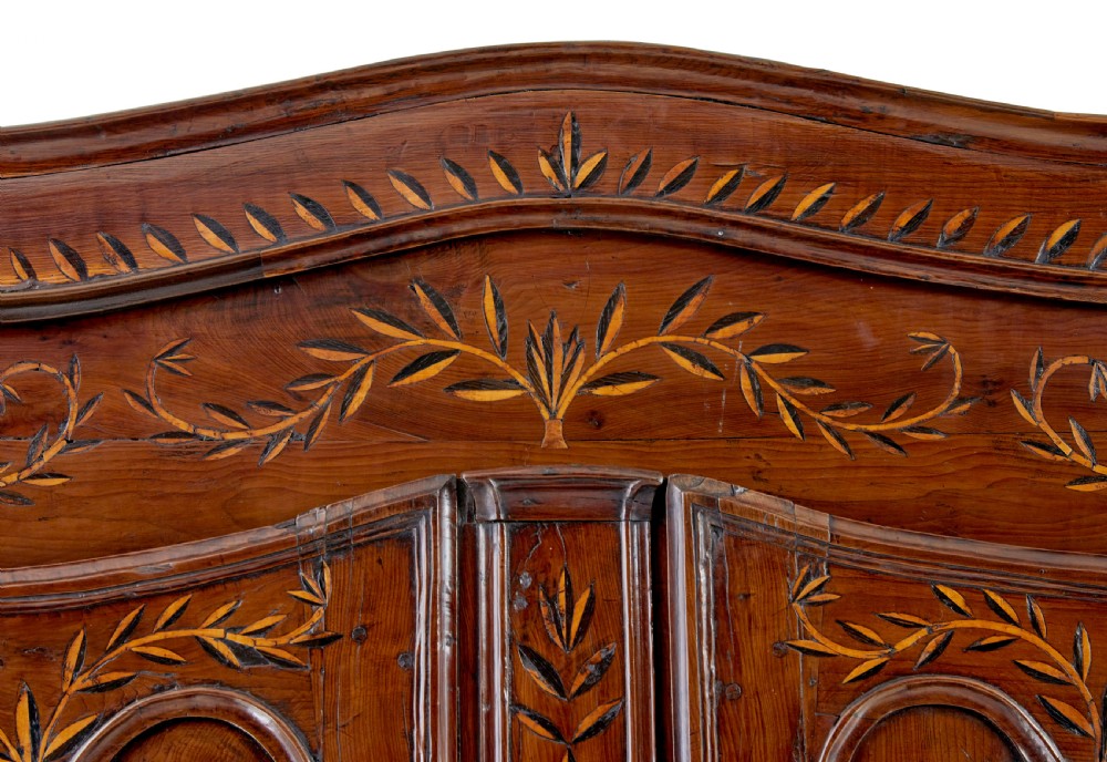 An 18th-century French armoire in warm brown yew and chestnut wood featuring carved foliate inlay, arched panel doors, and long iron escutcheons. View X