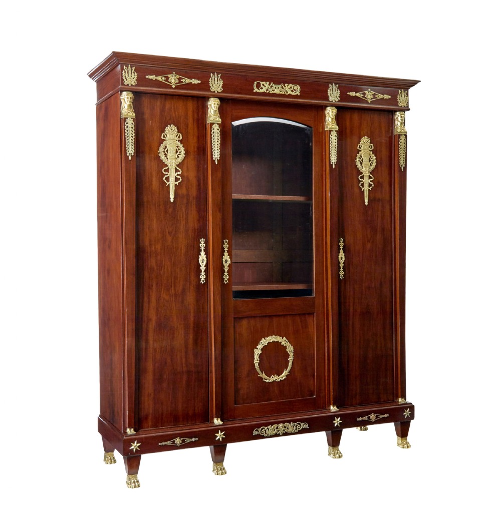 A late nineteenth-century French Empire style mahogany cabinet featuring three doors, central glass panelling, and ornate gold-coloured ormolu mounts.