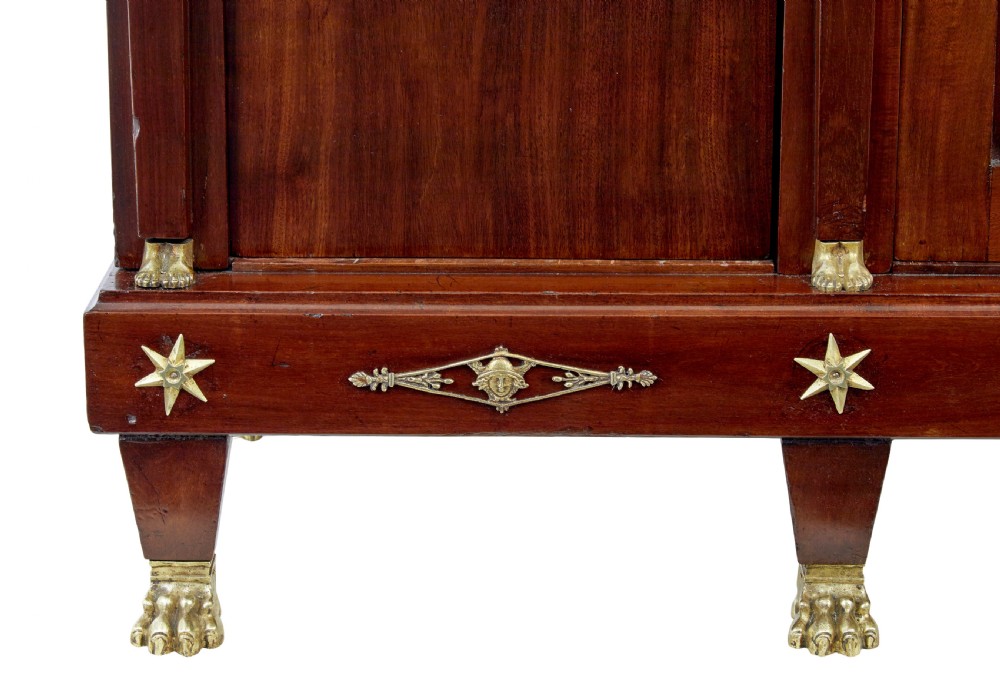 A late nineteenth-century French Empire style mahogany cabinet featuring three doors, central glass panelling, and ornate gold-coloured ormolu mounts. View X
