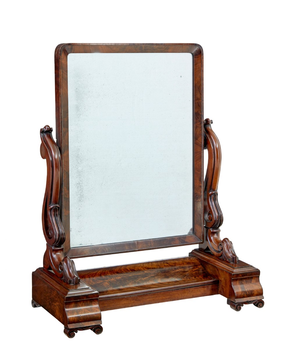 An Early Victorian mahogany toilet mirror featuring a rectangular frame set between carved scroll supports on a plinth base with scroll feet.