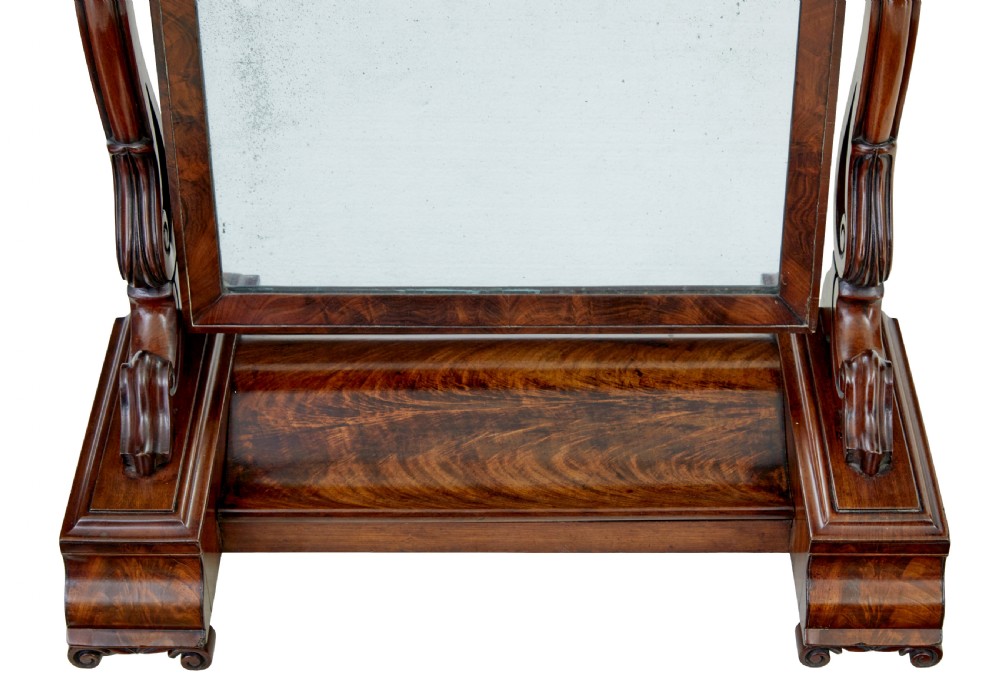 An Early Victorian mahogany toilet mirror featuring a rectangular frame set between carved scroll supports on a plinth base with scroll feet. View V