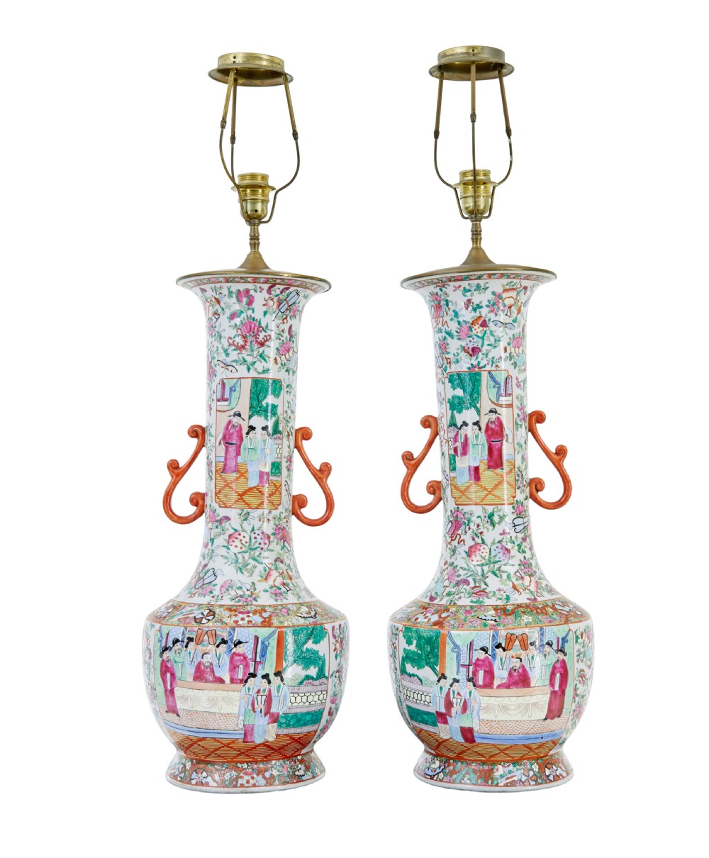A pair of large early 20th-century Chinese Cantonese porcelain vase lamps featuring hand-painted figurative panels, scroll handles, and brass light fittings.