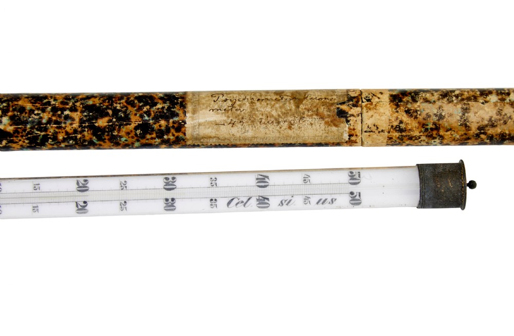 A 19th-century clear glass thermometer with printed measurement scales resting alongside its original brown marbled cylindrical paperboard storage tube. View II
