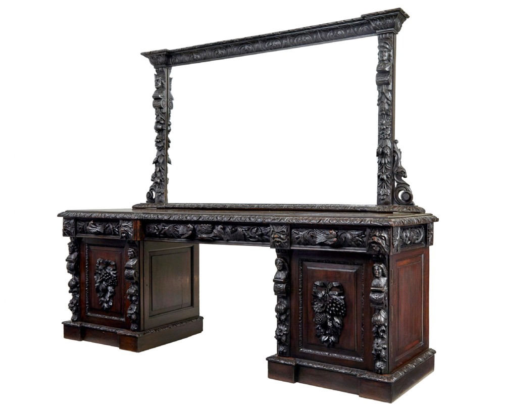 A 19th-century dark oak sideboard featuring twin carved pedestal cupboards, relief fruit swags, and an upper mirrored frame superstructure.