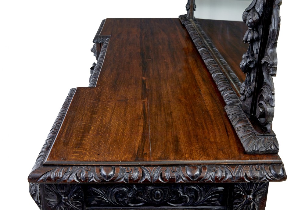 A 19th-century dark oak sideboard featuring twin carved pedestal cupboards, relief fruit swags, and an upper mirrored frame superstructure. View X