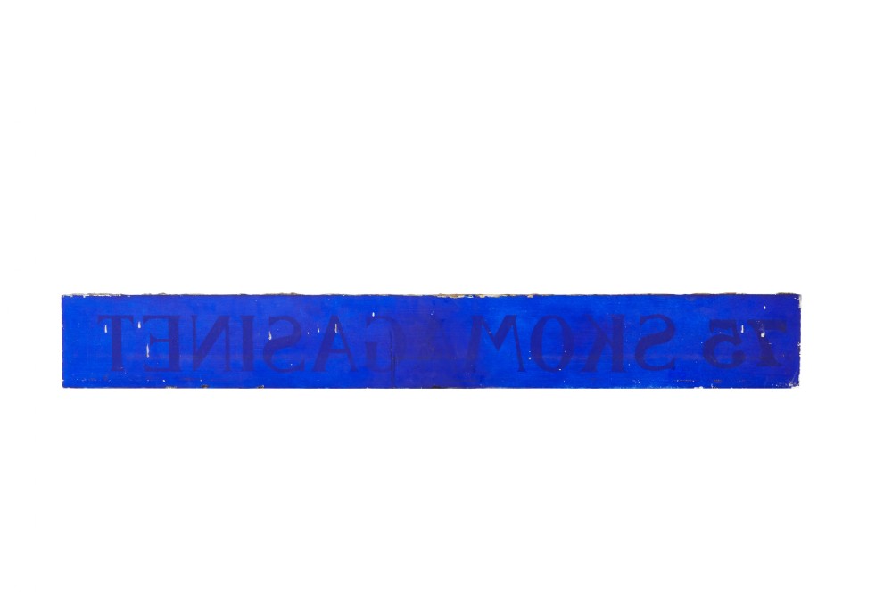 A long rectangular cobalt blue glass sign with gilded gold leaf lettering reading 75 SKOMAGASINET. View III