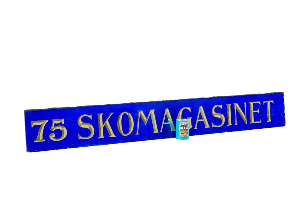 A long rectangular cobalt blue glass sign with gilded gold leaf lettering reading 75 SKOMAGASINET. View IV