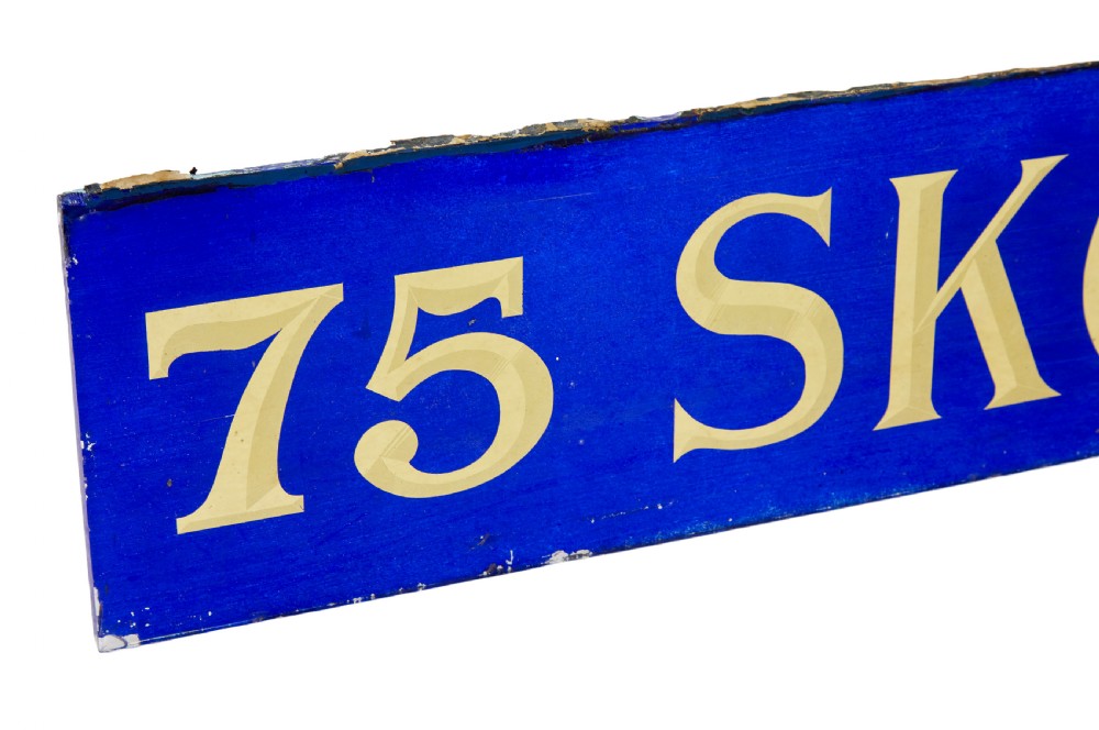 A long rectangular cobalt blue glass sign with gilded gold leaf lettering reading 75 SKOMAGASINET. View V