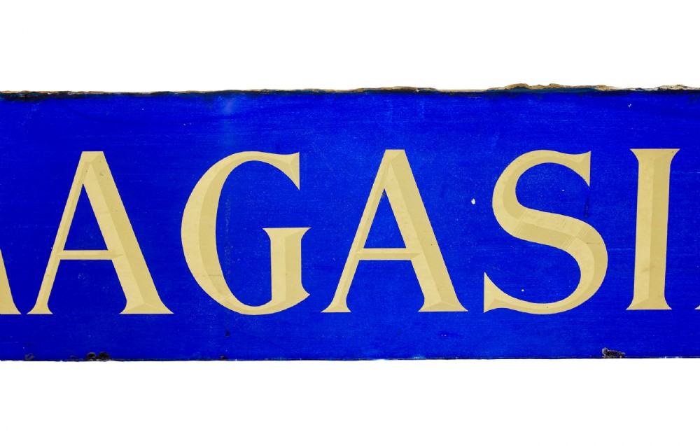 A long rectangular cobalt blue glass sign with gilded gold leaf lettering reading 75 SKOMAGASINET. View VI