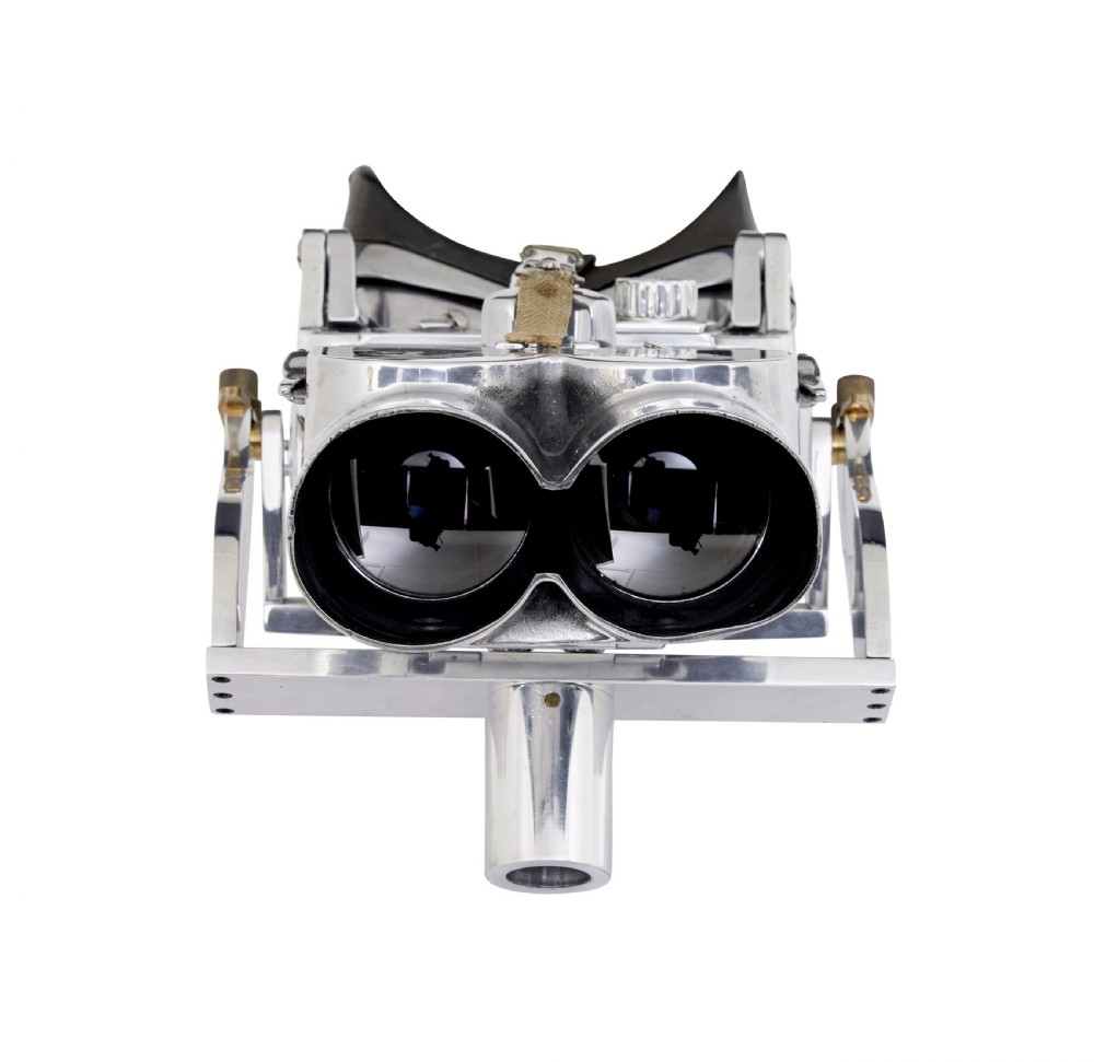 A pair of polished steel military binoculars mounted on a tall three-legged metal tripod stand against a plain background. View II