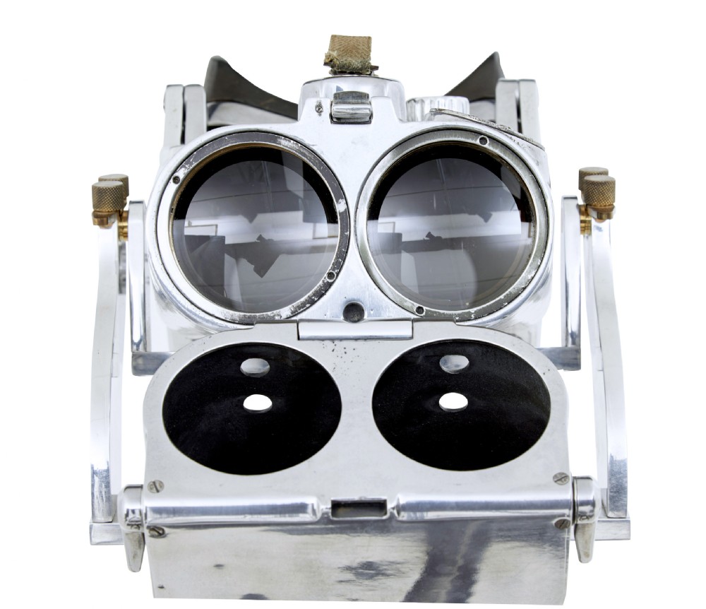 A pair of polished steel military binoculars mounted on a tall three-legged metal tripod stand against a plain background. View XV