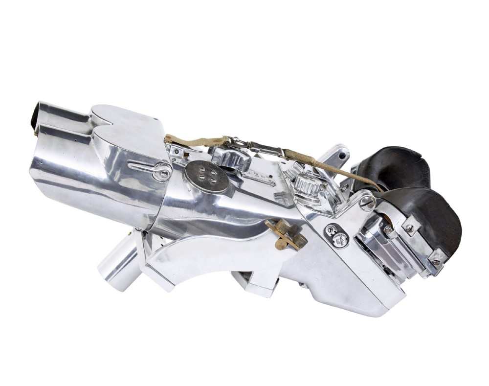 A pair of polished steel military binoculars mounted on a tall three-legged metal tripod stand against a plain background. View XVII