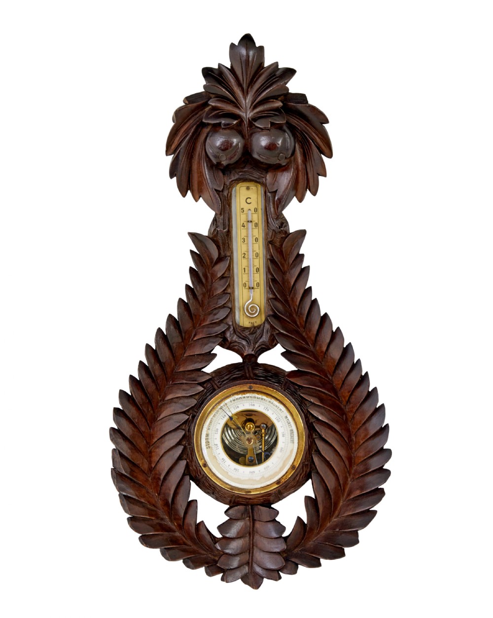 A 19th-century dark carved walnut aneroid wall barometer featuring foliate leaf carvings surrounding a central thermometer tube and a lower circular glass dial.