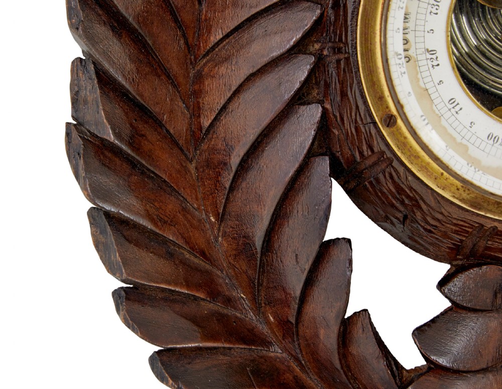 A 19th-century dark carved walnut aneroid wall barometer featuring foliate leaf carvings surrounding a central thermometer tube and a lower circular glass dial. View III