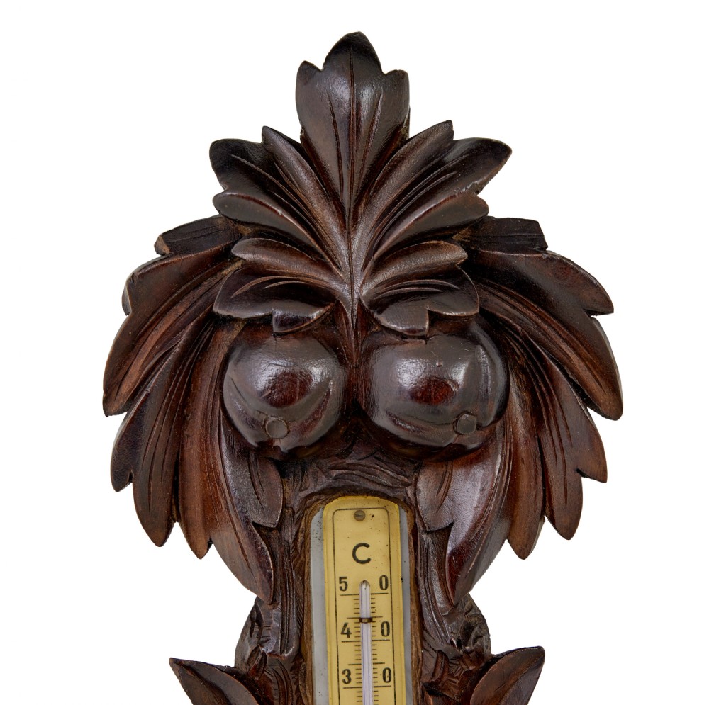 A 19th-century dark carved walnut aneroid wall barometer featuring foliate leaf carvings surrounding a central thermometer tube and a lower circular glass dial. View IV