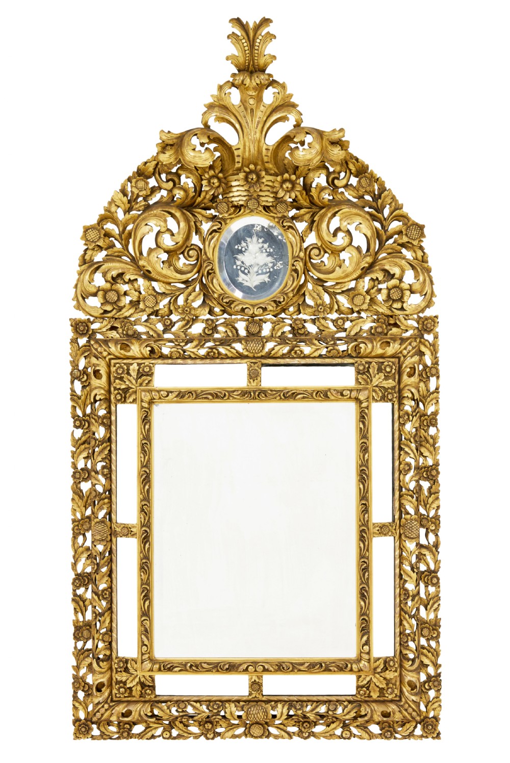 An ornate gold gilt wall mirror featuring a carved cushion frame decorated with floral motifs, scrollwork, and an etched oval glass crest.