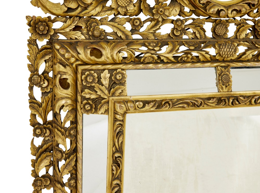 An ornate gold gilt wall mirror featuring a carved cushion frame decorated with floral motifs, scrollwork, and an etched oval glass crest. View IV