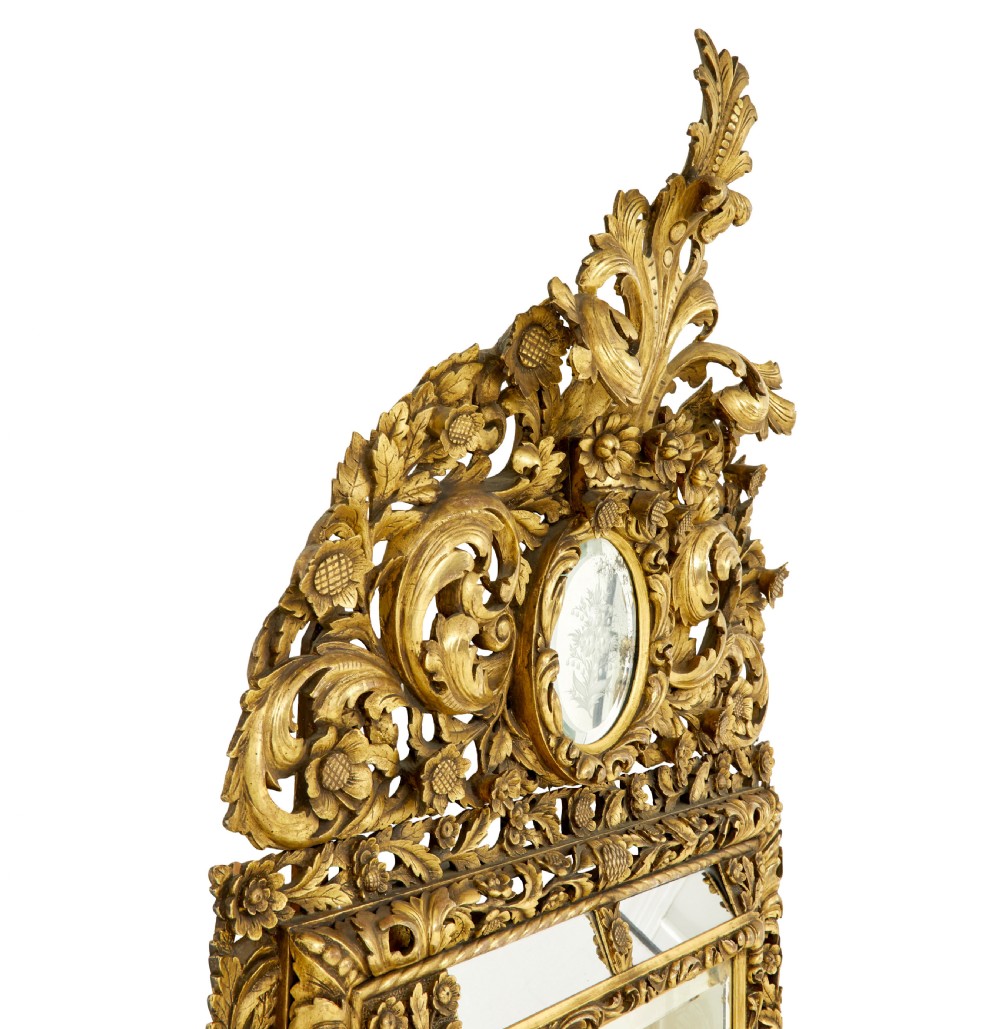 An ornate gold gilt wall mirror featuring a carved cushion frame decorated with floral motifs, scrollwork, and an etched oval glass crest. View V