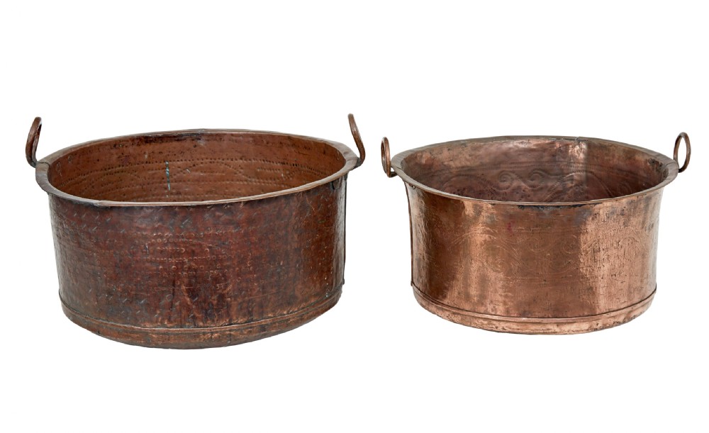 A pair of nineteenth-century hand-hammered copper cooking vessels featuring rolled rims, loop side handles, and chased decorative patterns around the bodies.