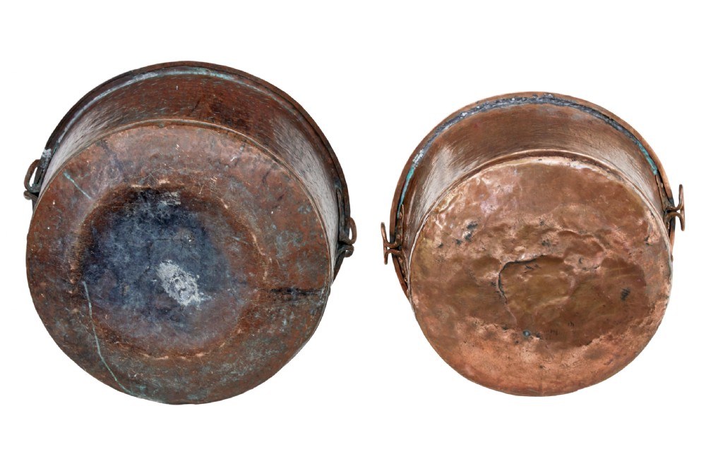 A pair of nineteenth-century hand-hammered copper cooking vessels featuring rolled rims, loop side handles, and chased decorative patterns around the bodies. View V