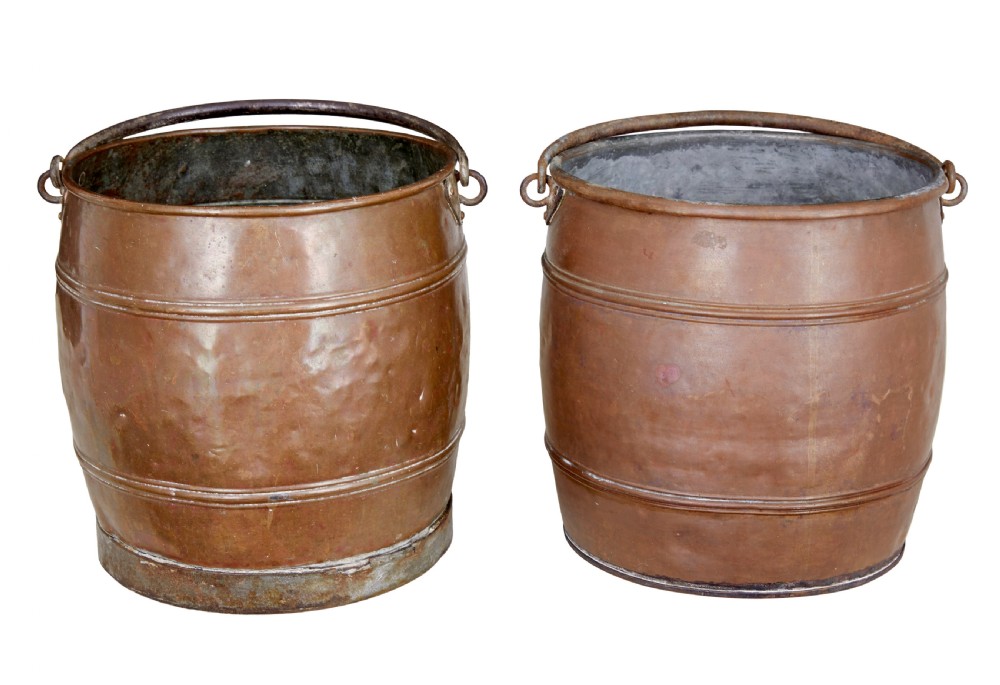 A near pair of late 19th-century cylindrical copper buckets featuring hand-hammered surfaces, reeded metal bands, and dark iron swing handles.