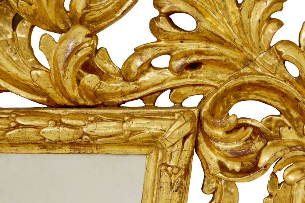 An 18th-century Italian Rococo wall mirror featuring an openwork carved giltwood frame decorated with acanthus leaf scrolls and a decorative cresting around a glass plate. View VI