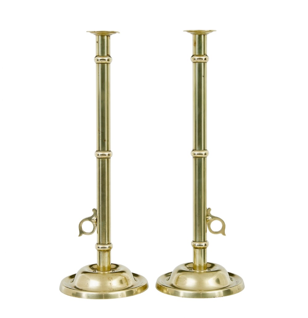 A pair of tall 19th-century Arts and Crafts polished brass candlesticks featuring tubular stems with knops, side loop handles, and domed bases.