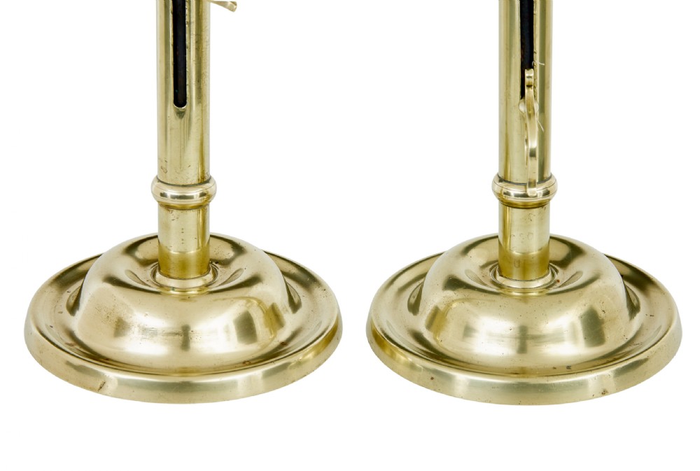 A pair of tall 19th-century Arts and Crafts polished brass candlesticks featuring tubular stems with knops, side loop handles, and domed bases. View IV