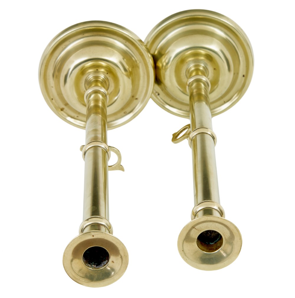 A pair of tall 19th-century Arts and Crafts polished brass candlesticks featuring tubular stems with knops, side loop handles, and domed bases. View VI
