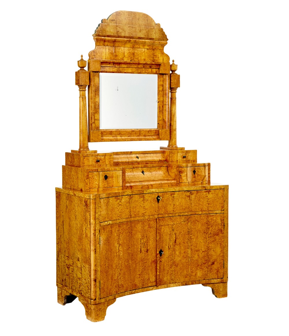 An early 19th-century Biedermeier vanity cabinet featuring a central framed mirror, stepped tier of small drawers, and a double-door base in figured golden birch timber.