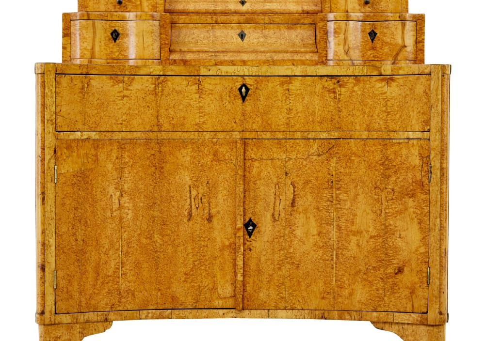 An early 19th-century Biedermeier vanity cabinet featuring a central framed mirror, stepped tier of small drawers, and a double-door base in figured golden birch timber. View IX