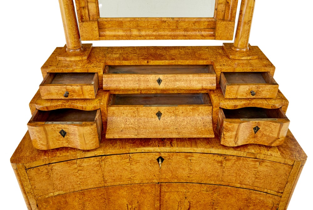 An early 19th-century Biedermeier vanity cabinet featuring a central framed mirror, stepped tier of small drawers, and a double-door base in figured golden birch timber. View XI