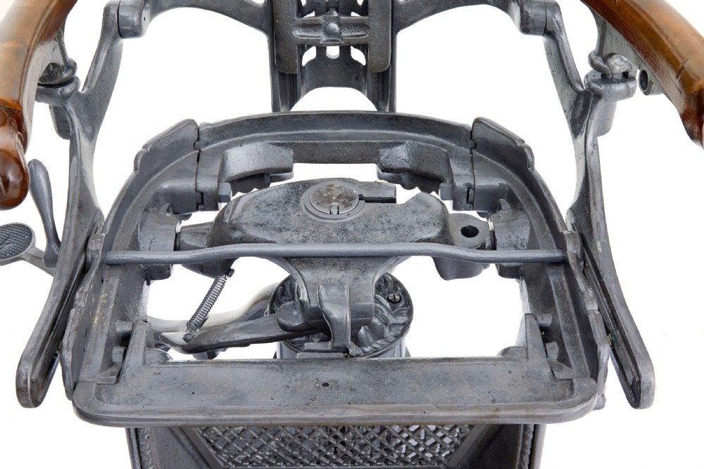 A 19th-century American cast iron dentist chair featuring an adjustable headrest, cream upholstered seat, wooden armrests, and footrest supported by clawed iron feet. View II