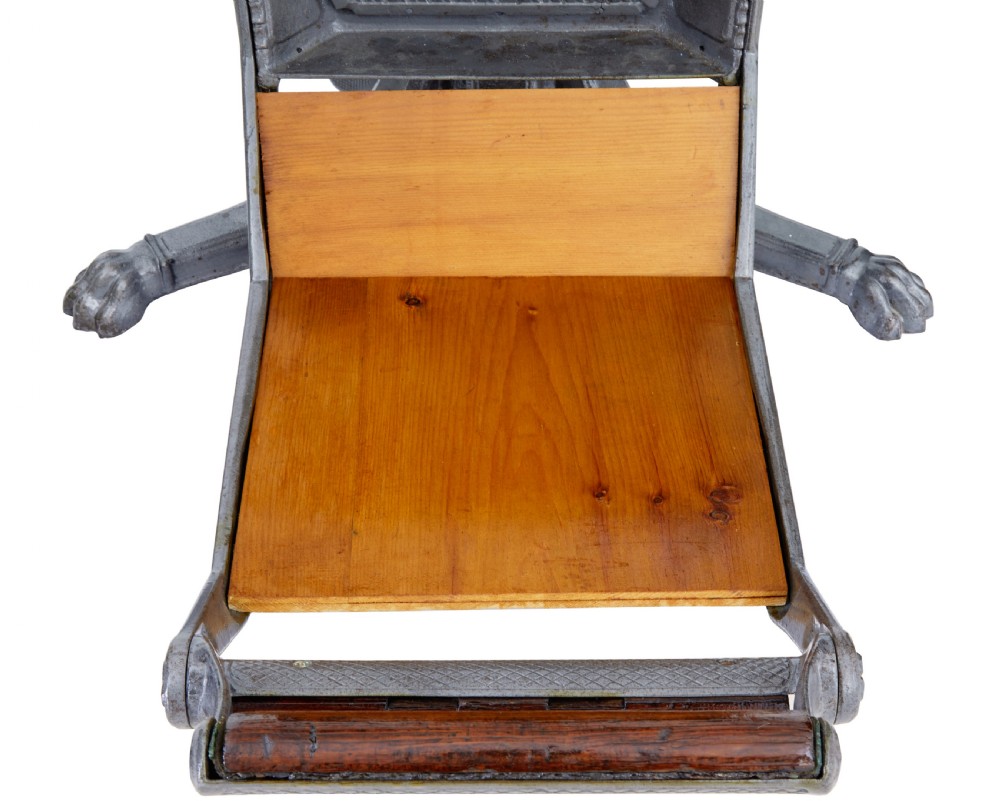A 19th-century American cast iron dentist chair featuring an adjustable headrest, cream upholstered seat, wooden armrests, and footrest supported by clawed iron feet. View IV
