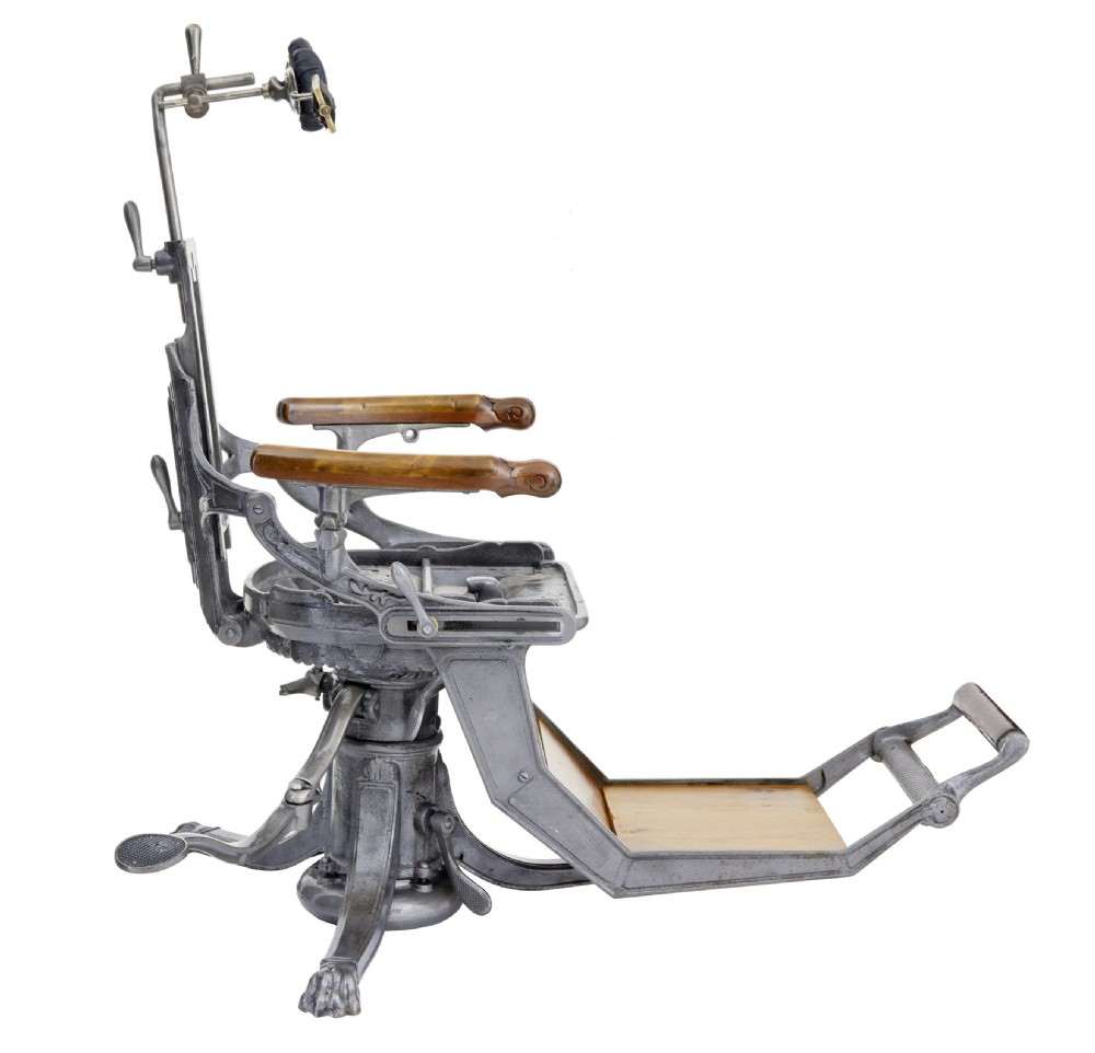A 19th-century American cast iron dentist chair featuring an adjustable headrest, cream upholstered seat, wooden armrests, and footrest supported by clawed iron feet. View VIII