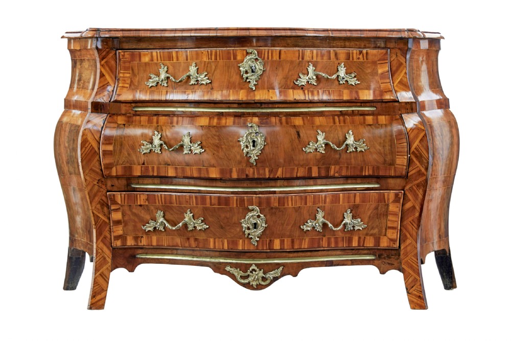 An early nineteenth-century walnut bombe commode featuring three curved drawers with parquetry inlay and ornate brass handles.
