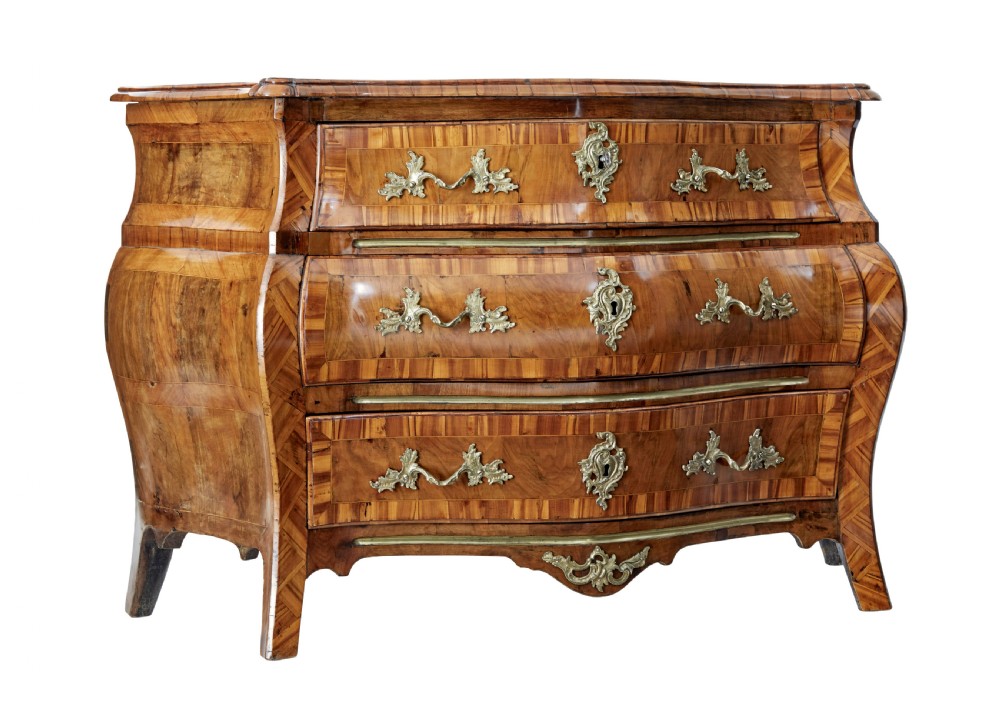 An early nineteenth-century walnut bombe commode featuring three curved drawers with parquetry inlay and ornate brass handles. View II