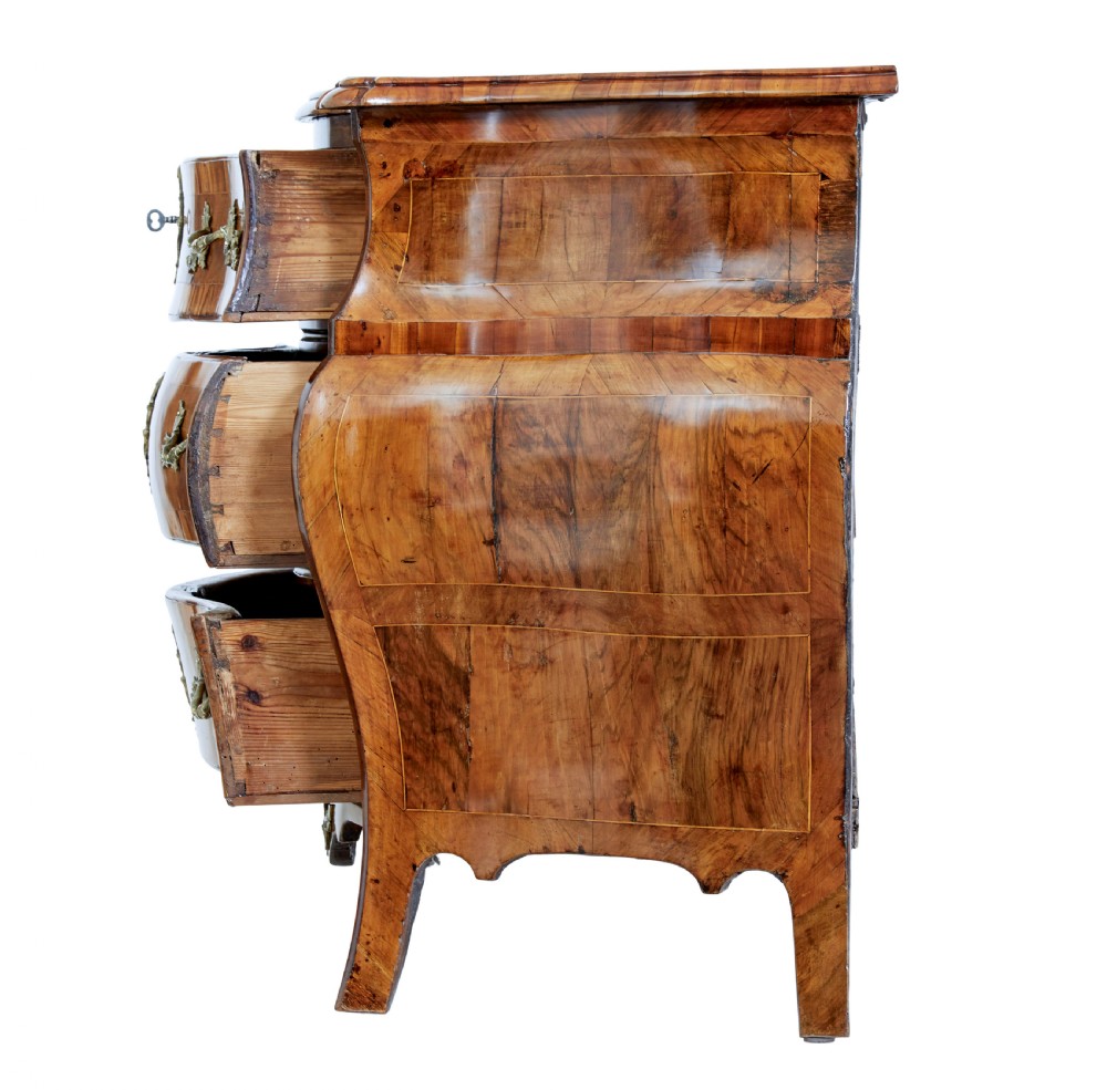 An early nineteenth-century walnut bombe commode featuring three curved drawers with parquetry inlay and ornate brass handles. View V