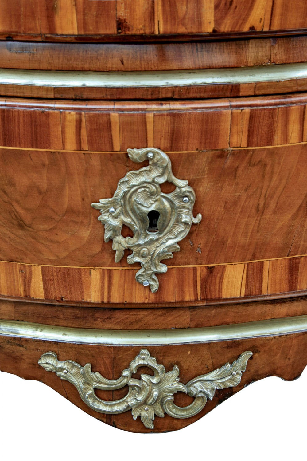 An early nineteenth-century walnut bombe commode featuring three curved drawers with parquetry inlay and ornate brass handles. View X