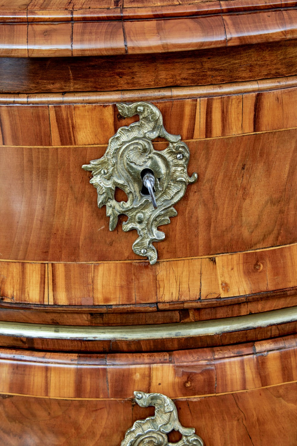 An early nineteenth-century walnut bombe commode featuring three curved drawers with parquetry inlay and ornate brass handles. View XI