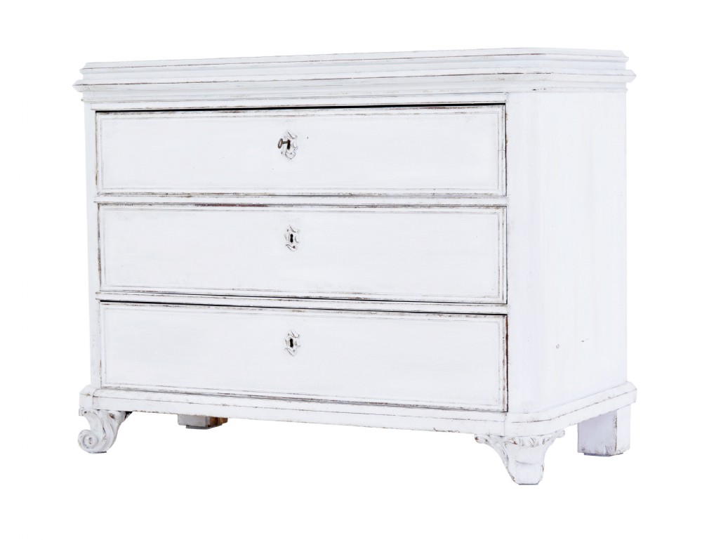 A 19th-century Swedish chest of drawers featuring three long drawers with central escutcheons and a distressed white painted finish resting on carved feet.