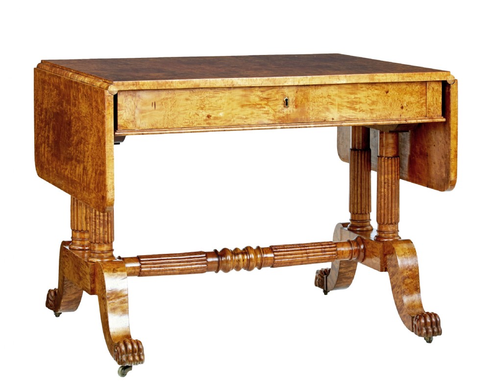 A nineteenth-century Biedermeier burr birch sofa table featuring twin drop leaves, a frieze drawer, fluted column supports, a turned central stretcher, and carved paw feet on castors.