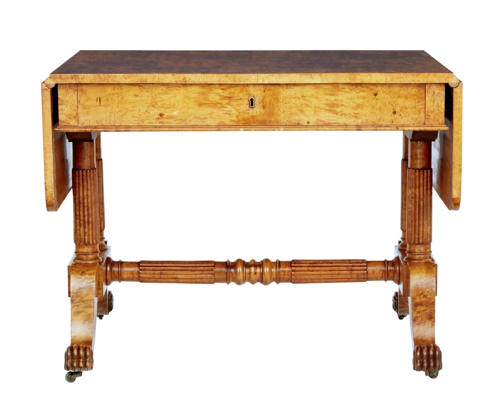 A nineteenth-century Biedermeier burr birch sofa table featuring twin drop leaves, a frieze drawer, fluted column supports, a turned central stretcher, and carved paw feet on castors. View II